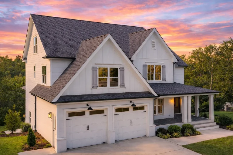 Front exterior view of a New American Modern Traditional farmhouse home with white board and batten siding, steep gables, covered porch, and attached garage
