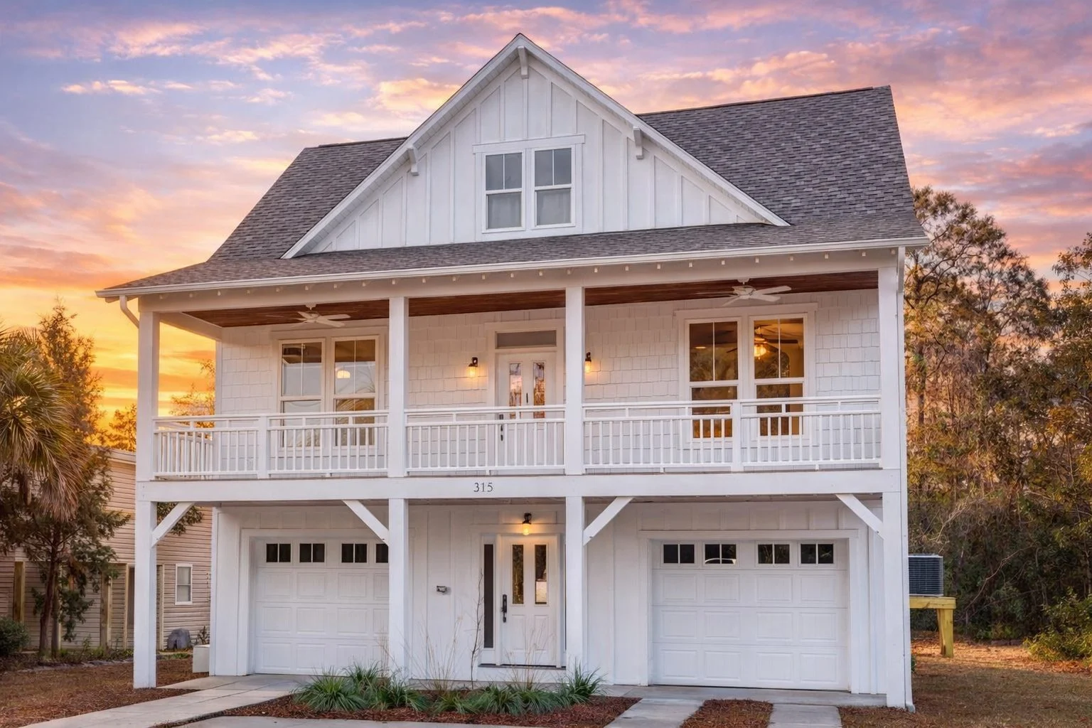 Front elevation of Low Country Coastal style home with board and batten siding, double stacked porches, elevated garage, and symmetrical Charleston-inspired design