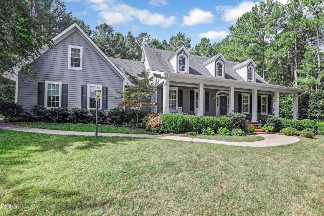 Front view of a Traditional Colonial Cape Cod style house featuring white horizontal siding, black shutters, brick foundation, and a welcoming front porch with dormers.