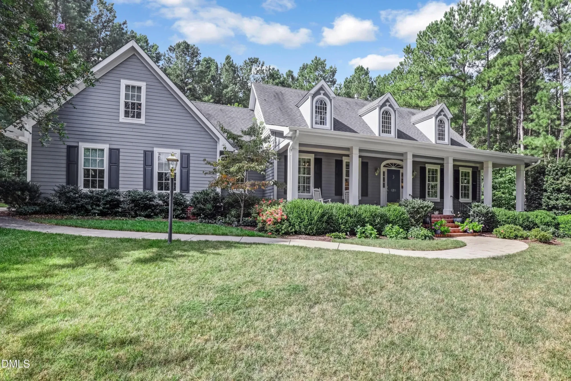 Front view of a Traditional Colonial Cape Cod style house featuring white horizontal siding, black shutters, brick foundation, and a welcoming front porch with dormers.