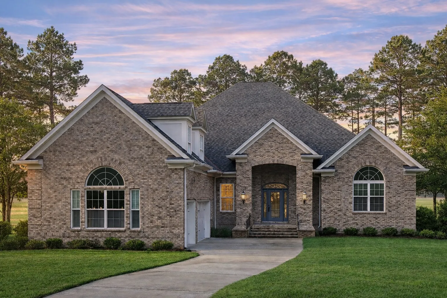 Front elevation of a Traditional New American house with brick water table, smooth stucco walls, arched windows, shutters, and a centered entry