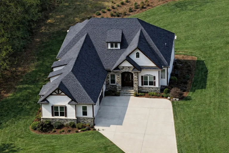 Front exterior of French Country style home with stone and stucco facade, steep hip roof, arched entry, and side-entry garage