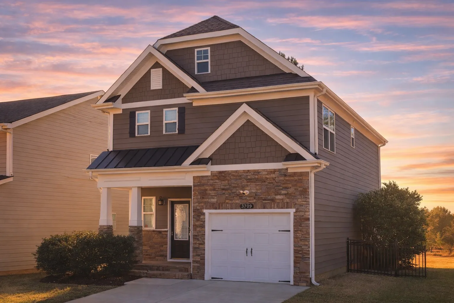 Front elevation of a Traditional New American style home with beige siding, stone accents, and black shutters under a gabled roof