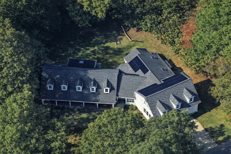 Front exterior view of a Modern Farmhouse home with navy-blue siding, red doors, dormers, and covered porch showcasing Colonial design influence