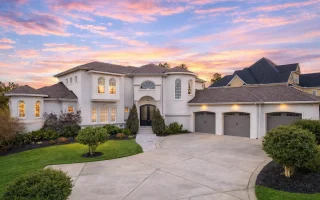 Front exterior of a luxury Neo-Classical style home featuring smooth stucco walls, arched windows, symmetrical façade, and a three-car garage