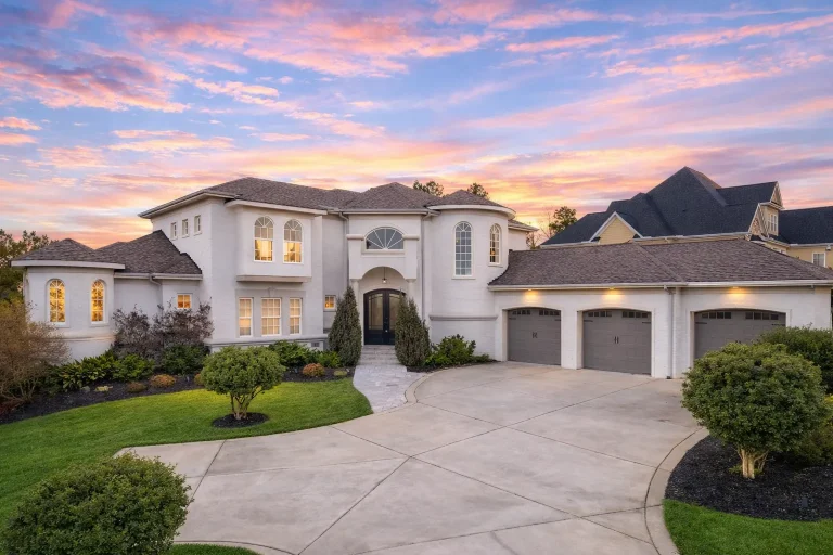 Front exterior of a luxury Neo-Classical style home featuring smooth stucco walls, arched windows, symmetrical façade, and a three-car garage