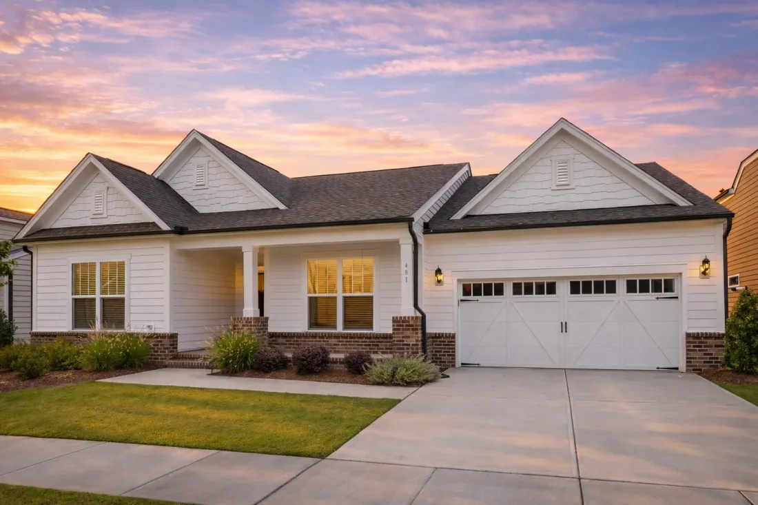 Front exterior of a Cape Cod style traditional home featuring horizontal siding, stone accents, dormer windows, and a two-car garage