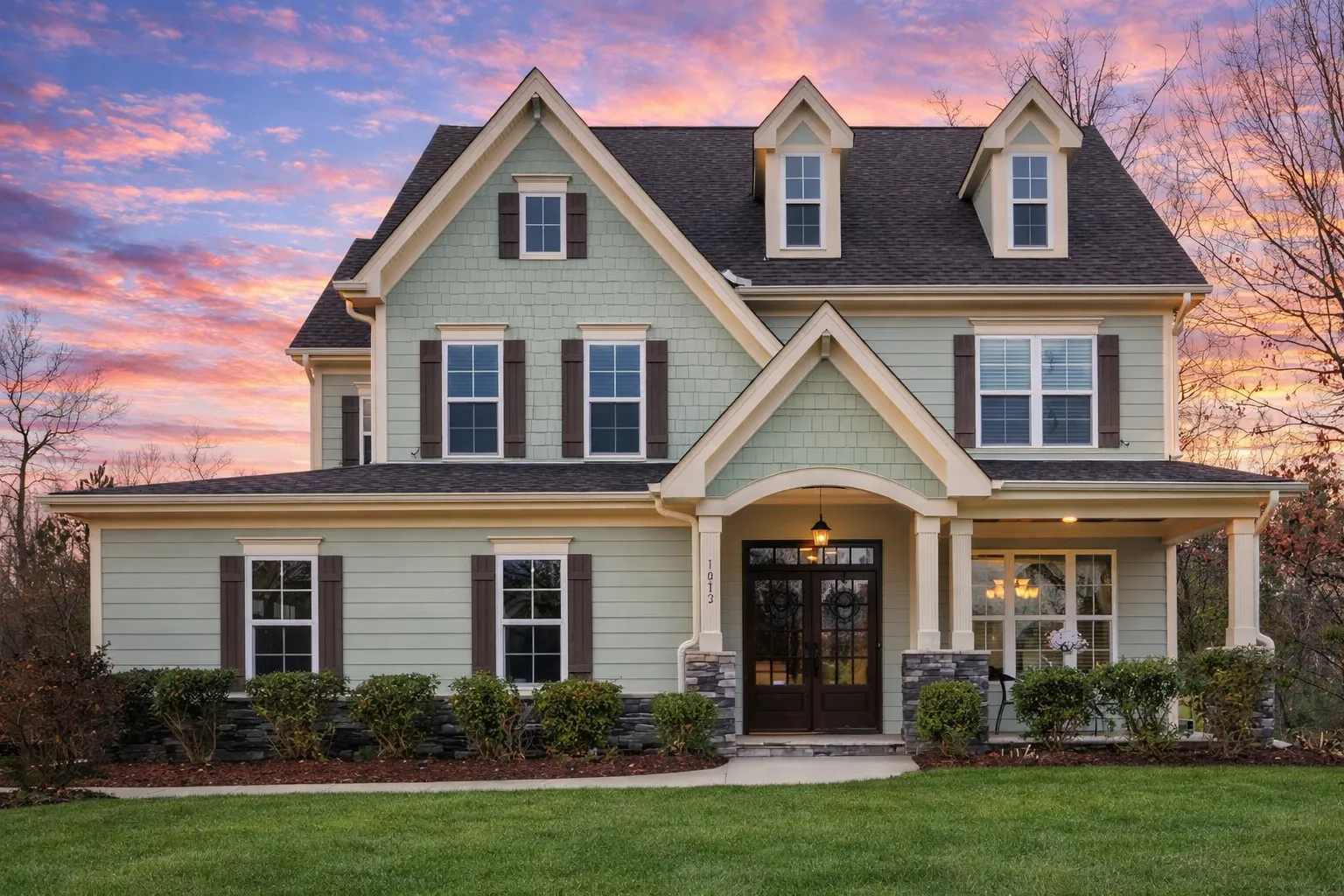 Front elevation of a Modern Farmhouse style home featuring board and batten siding, stone entry arch, black shutters, and symmetrical New American design