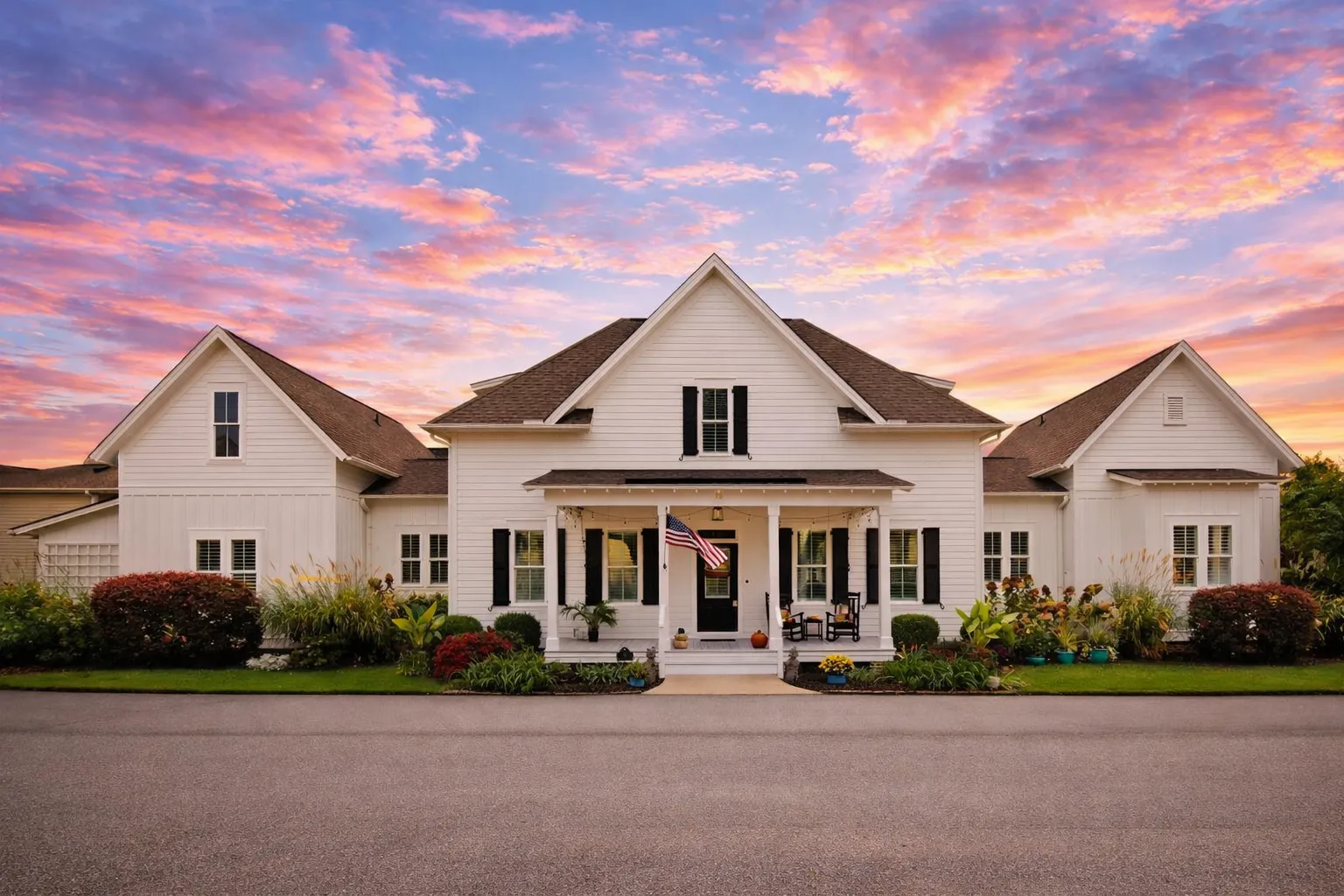 Front view of a Modern Farmhouse style home with white board and batten siding, brick porch piers, black metal porch roof, and gable dormers