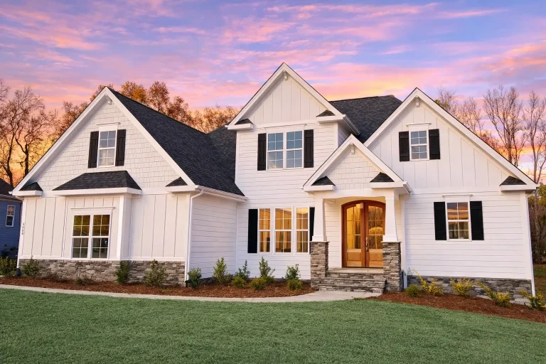 Front elevation of a Traditional Colonial home featuring horizontal siding, black shutters, and a stone accent wall with symmetrical windows and gable rooflines.