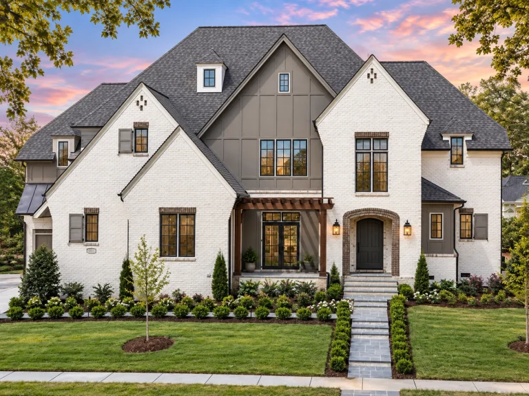 Front exterior view of a French Country style home featuring painted brick walls, board-and-batten gables, steep rooflines, and an arched entry