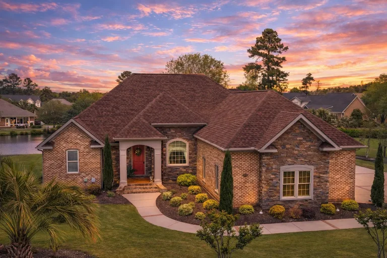 Front elevation of a French Country Traditional Suburban style home featuring light stone exterior, green shutters, and steep hip rooflines