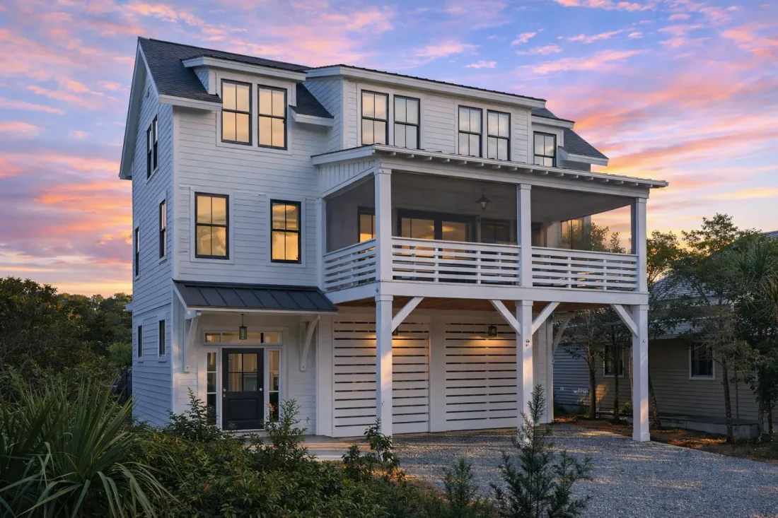 Front view of an elevated Coastal Modern Farmhouse featuring horizontal siding, large black-framed windows, and a double garage beneath covered balconies