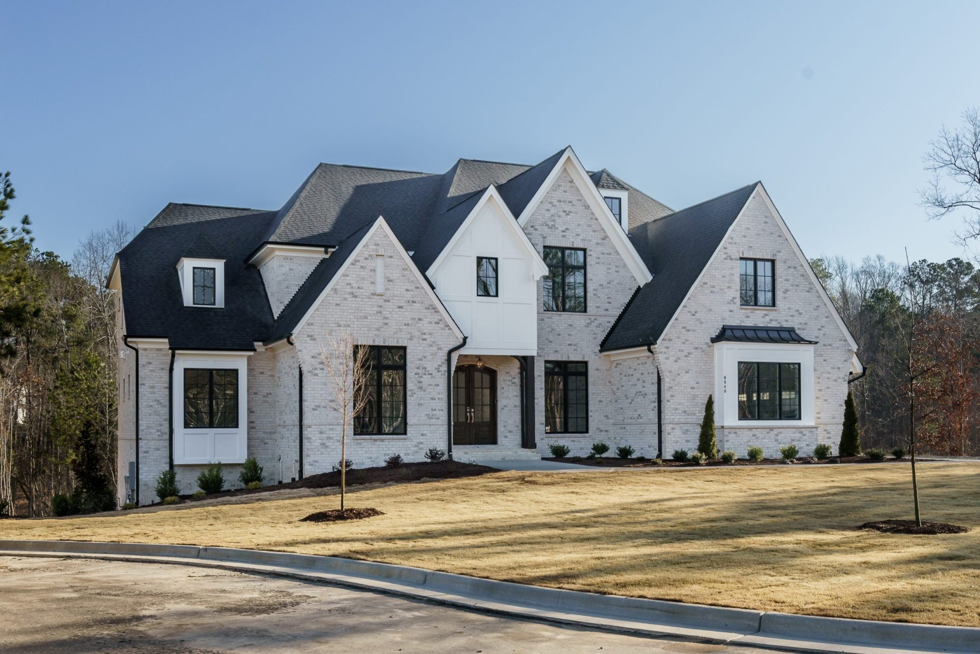 Front exterior of a New American Modern Traditional home featuring painted brick, stone accents, steep gables, and symmetrical architecture