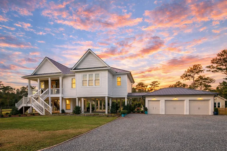 Front elevation of a Coastal Low Country style home with elevated foundation, horizontal siding, covered porch, and detached garage