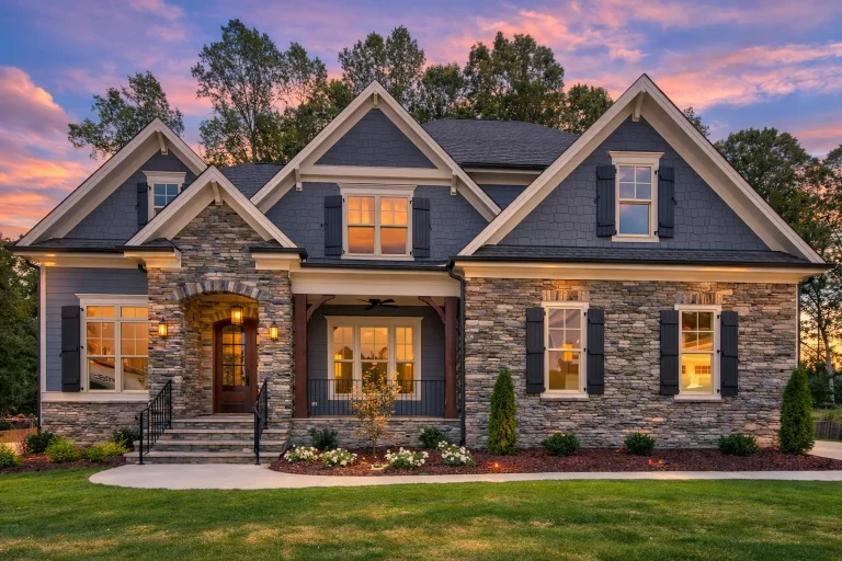 Front elevation of luxury Craftsman style home with stone veneer, horizontal lap siding, gabled rooflines, and covered porch at sunset