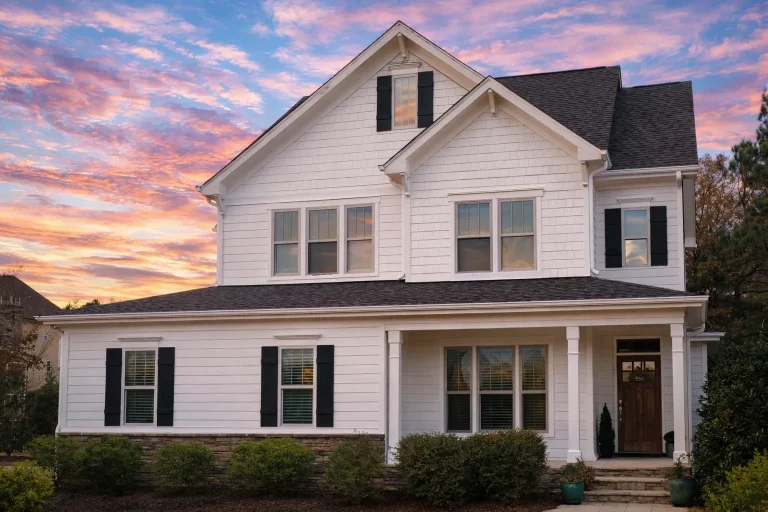 Front elevation of a New American style farmhouse home with white horizontal siding, stone foundation accents, black shutters, and a covered front porch