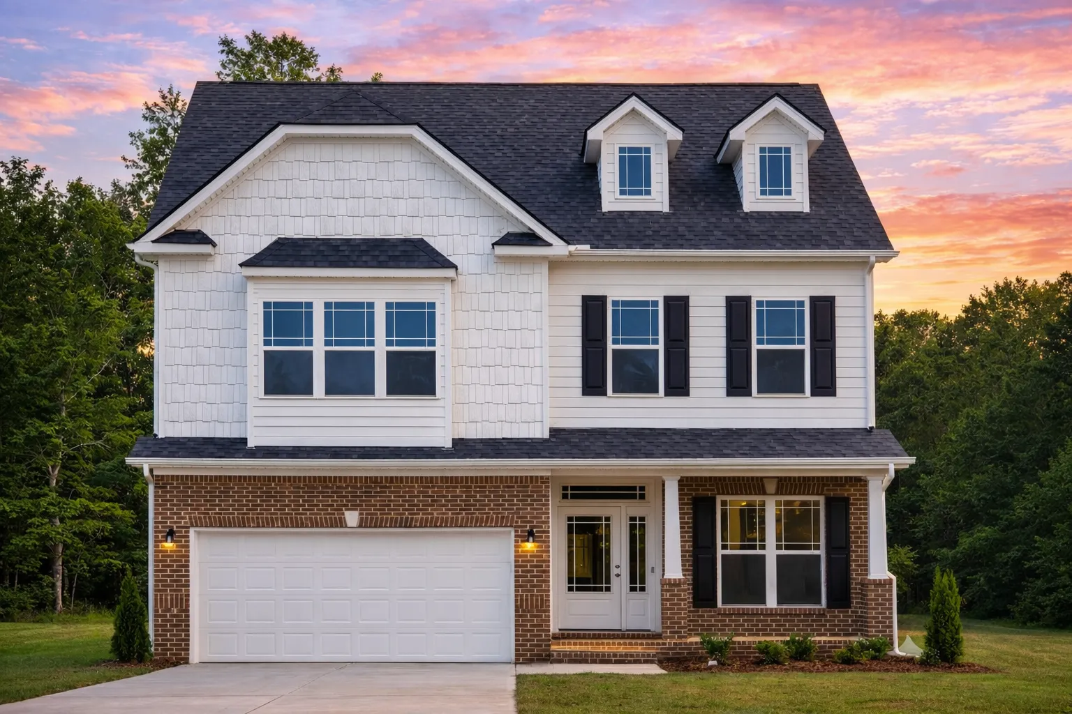 Front view of a two-story Traditional Colonial home featuring horizontal siding, shingle accents, and stone detailing with symmetrical windows and a double garage.