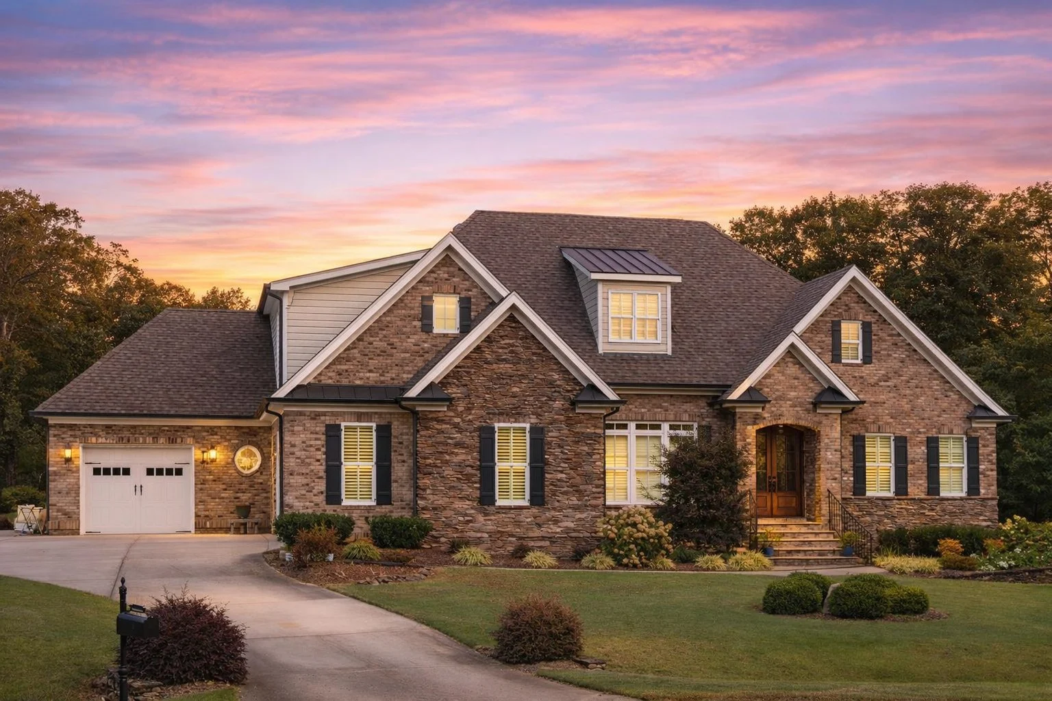 Front elevation of French Country style home with stone exterior, shake gables, arched entry, and side-entry garage