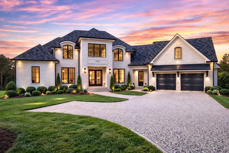 Front elevation of a French Country style luxury home with painted brick exterior, stone accents, steep rooflines, and arched windows