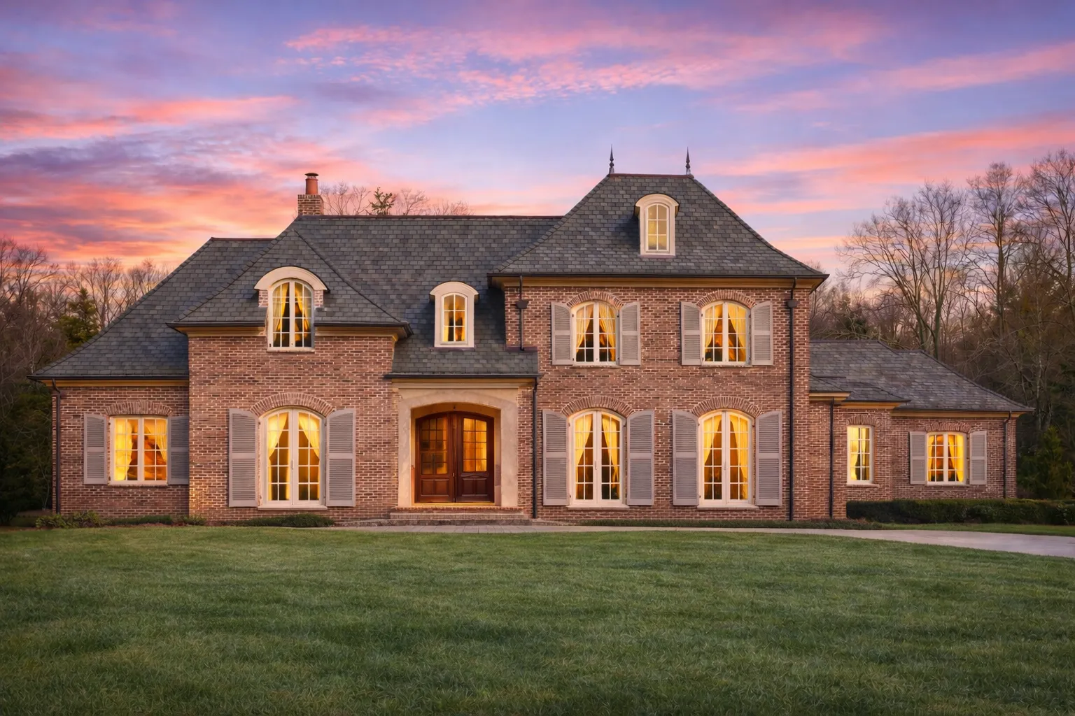 Front elevation of a French Provincial style home featuring brick exterior, steep hip rooflines, and traditional shuttered windows