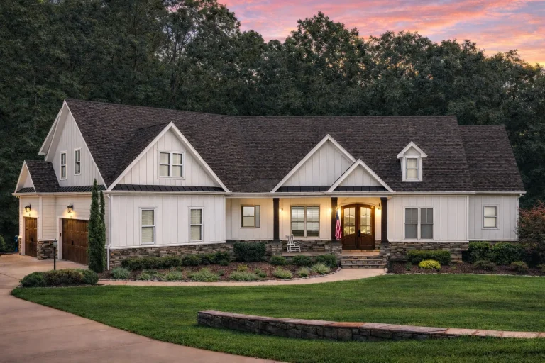 Front exterior of Southern Farmhouse ranch-style home with white lap siding, stone base accents, gabled rooflines, and covered front porch