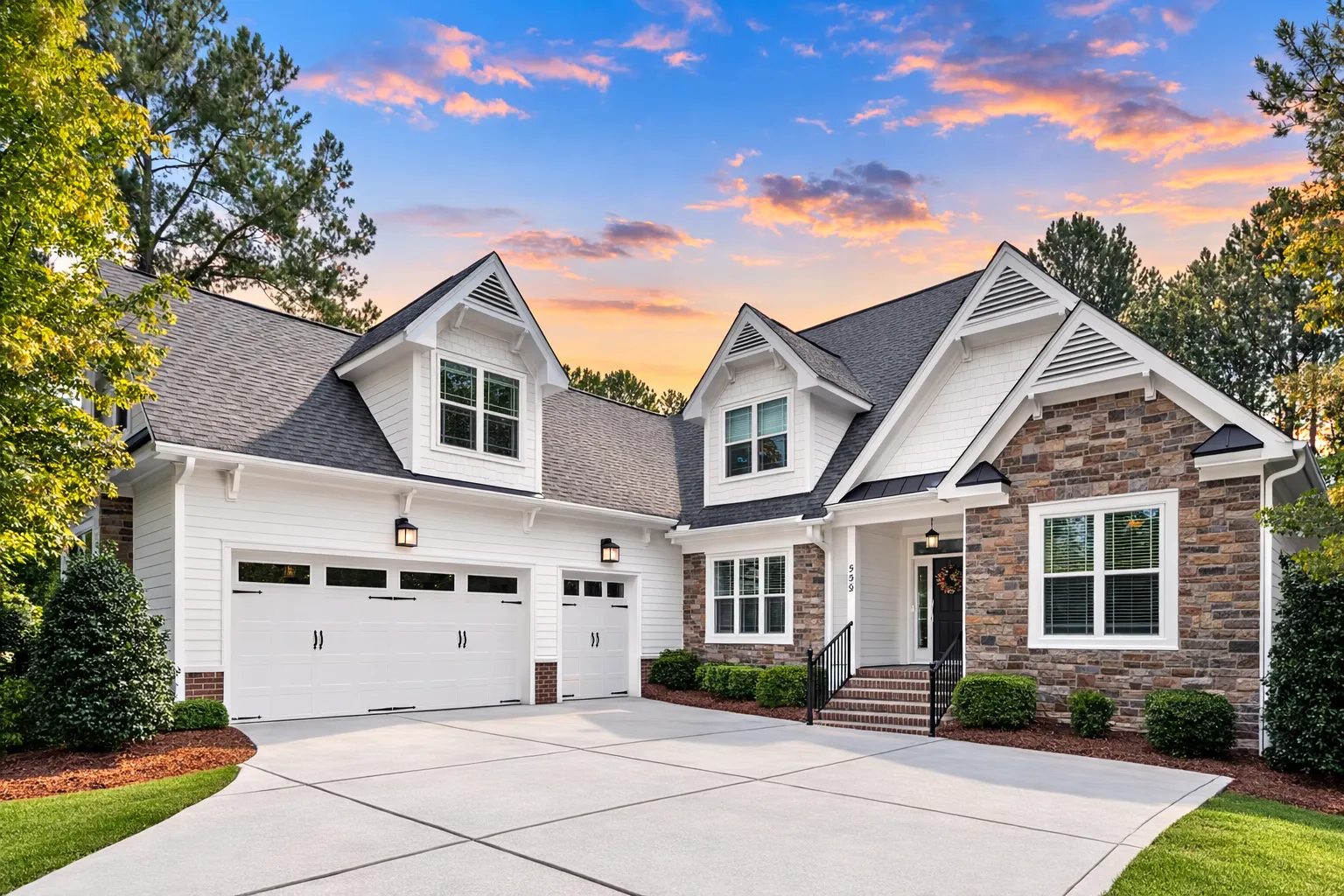 Front exterior of a Cape Cod cottage style home with horizontal siding, stone accents, steep gabled roof, and inviting red front door at sunset