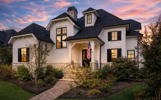 Front elevation of a French Country style luxury home featuring stone and stucco exterior, steep hipped roof, arched entry, and classic European detailing
