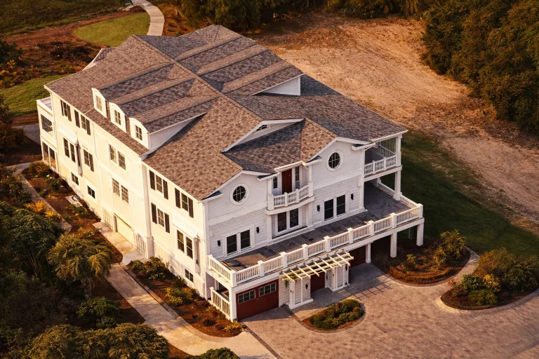 Aerial view of a Coastal Traditional home featuring shingle style siding, elevated foundation, expansive balconies, and classic Low Country architecture