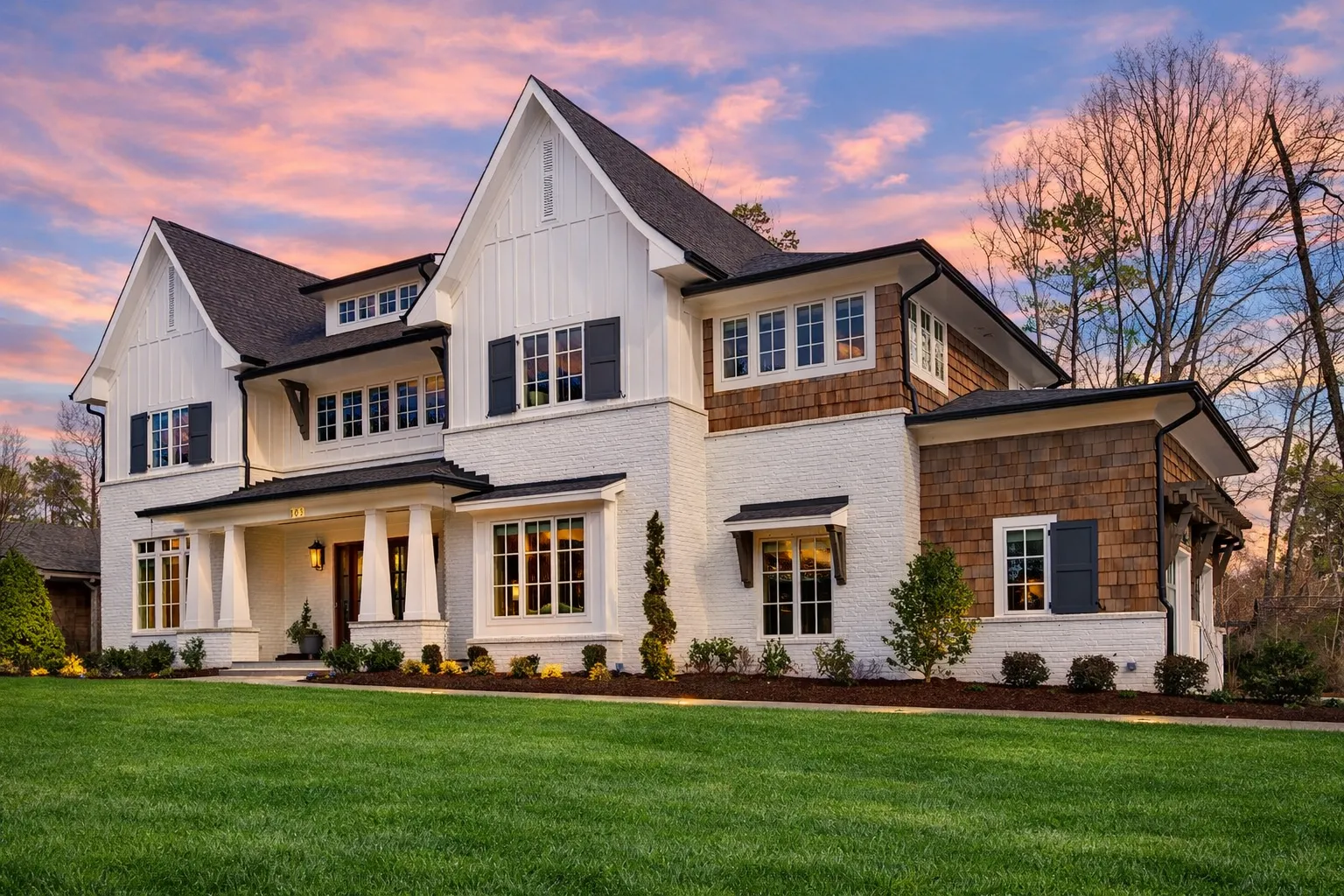 Front view of a Modern Farmhouse style home featuring a blend of stone and board and batten siding with gabled rooflines and black-framed windows