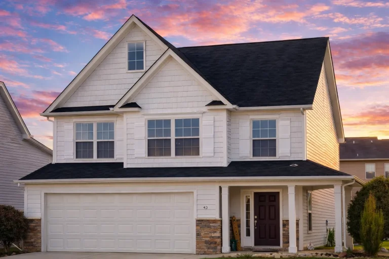 Front exterior of a Neo-Colonial style two-story suburban home with white lap siding, stone accents, black shingle roof, and attached two-car garage