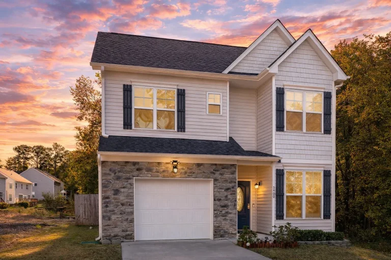 Front exterior of a New American style two-story home with blue horizontal siding, stone accents, white trim, and an attached garage