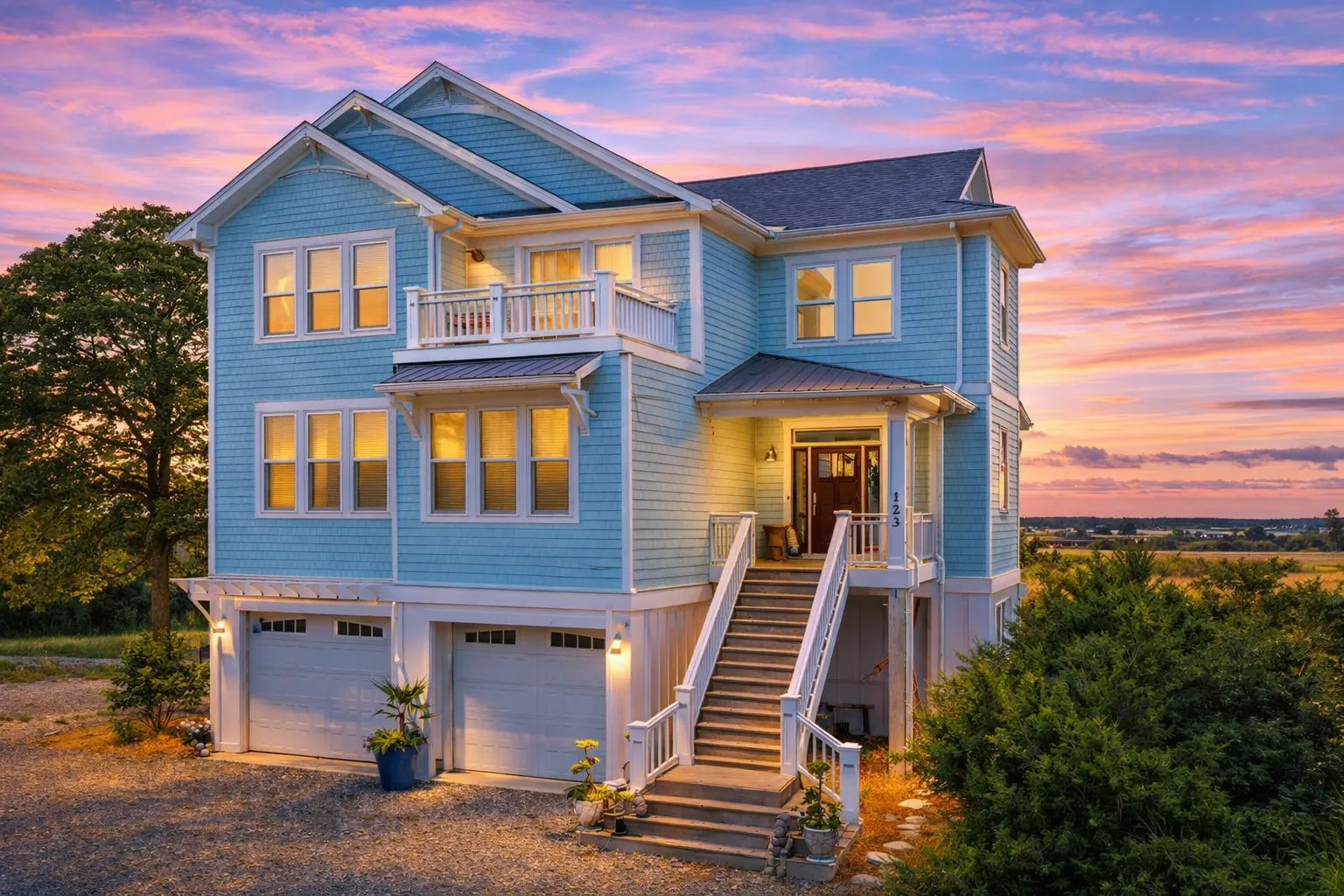 Front exterior view of an elevated coastal beach house with blue lap siding, covered porches, exterior stair entry, and garage below designed for flood-prone coastal living