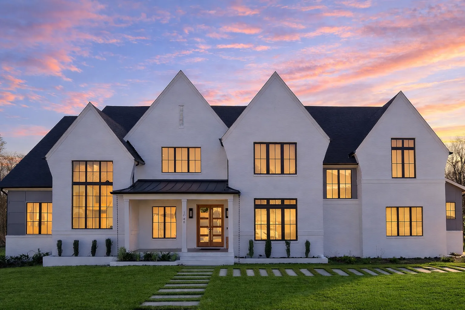 Front elevation of a Modern Farmhouse and New American style home with painted brick exterior, steep gable rooflines, black framed windows, and covered front porch