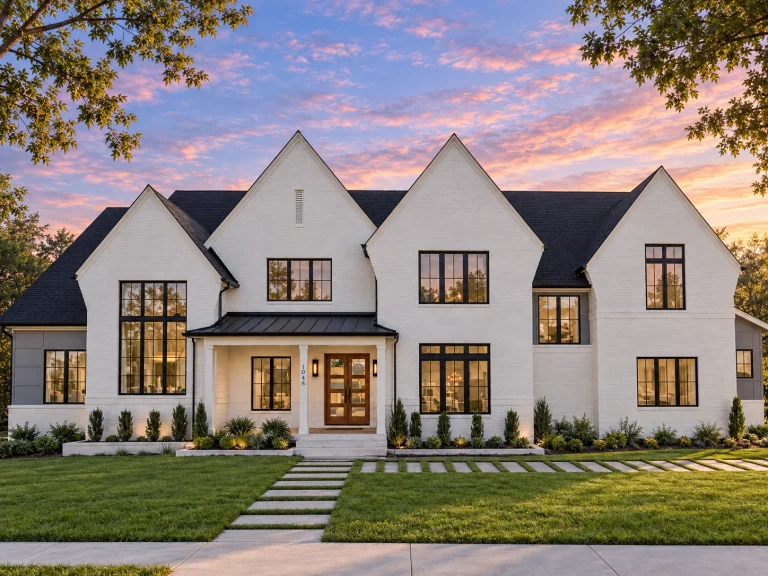 Front elevation of a Modern Farmhouse and New American style home with painted brick exterior, steep gable rooflines, black framed windows, and covered front porch