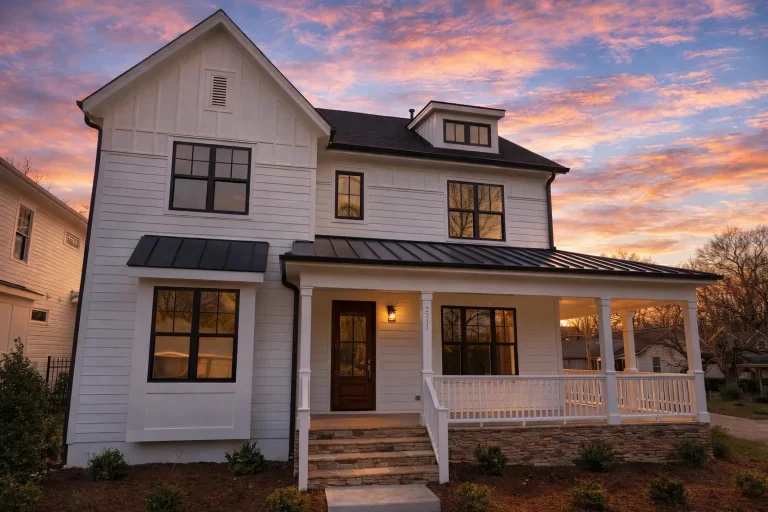 Front elevation of a modern farmhouse with white horizontal lap siding, black windows, covered porch, and standing seam metal roof at sunset