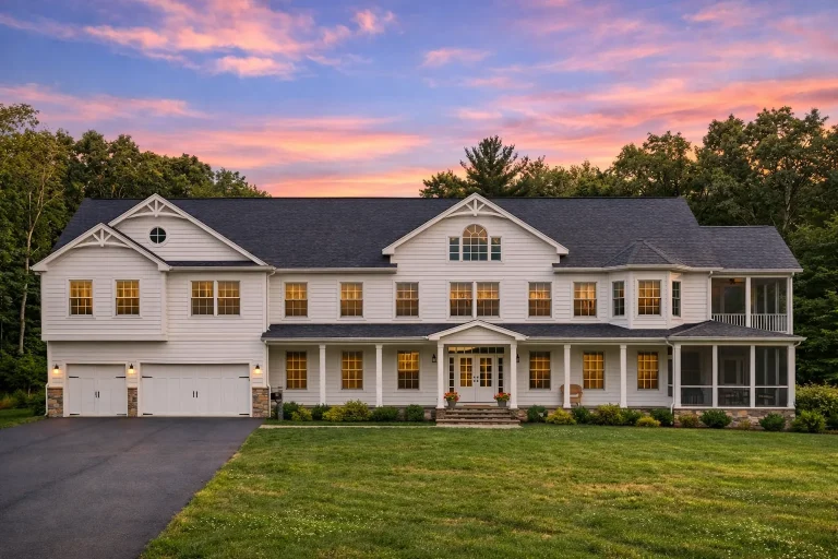 Front elevation of a large Colonial Revival style home with symmetrical façade, horizontal siding, stone foundation accents, and attached garage