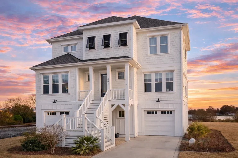 Front exterior of elevated coastal beach house with horizontal lap siding, double stair entry, covered porch, and ground-level garages