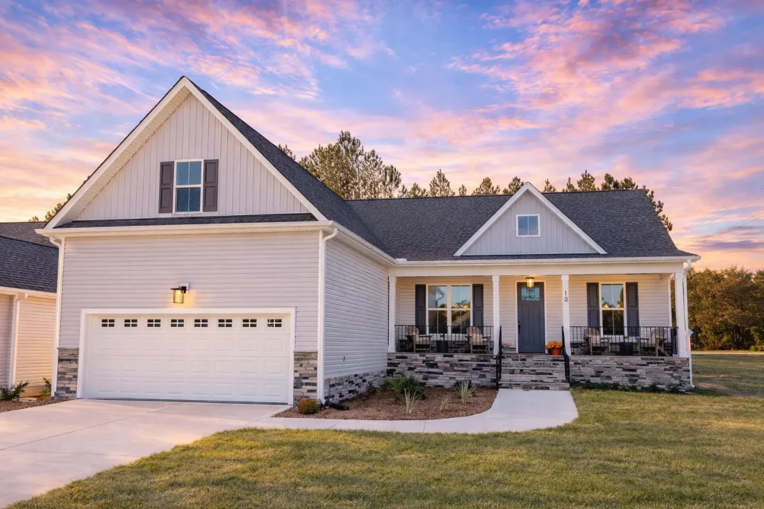 Front view of a Cape Cod Ranch style home with board and batten, horizontal siding, and stone accents featuring a green garage door and covered porch.