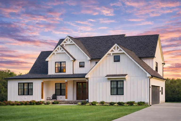Front elevation of a Modern Farmhouse style home featuring white board and batten siding, dark rooflines, stone foundation accents, and covered porch
