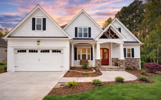 Front elevation of New American shingle style house with stone entry, lap siding, double garage, and Craftsman-inspired rooflines