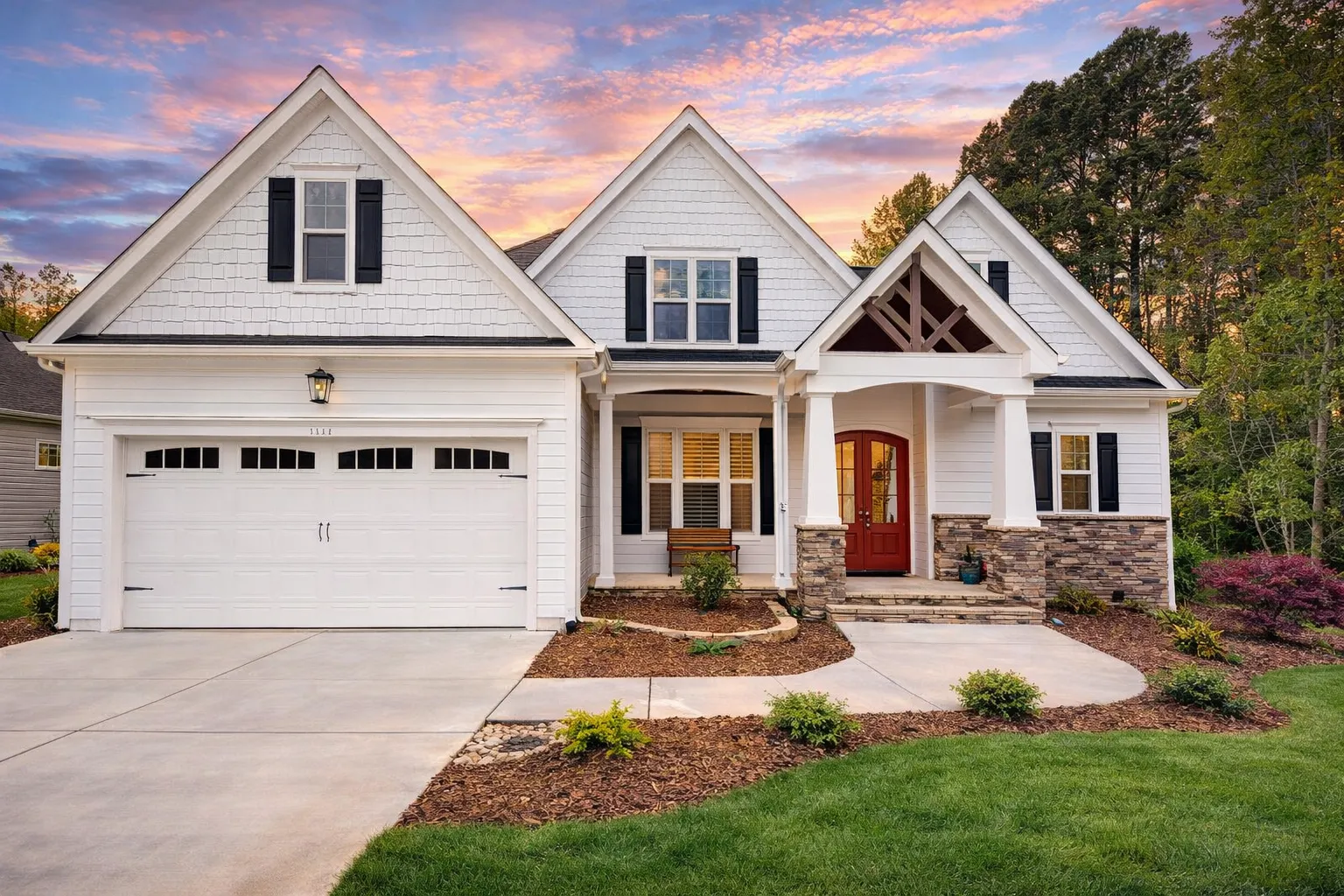 Front elevation of New American shingle style house with stone entry, lap siding, double garage, and Craftsman-inspired rooflines