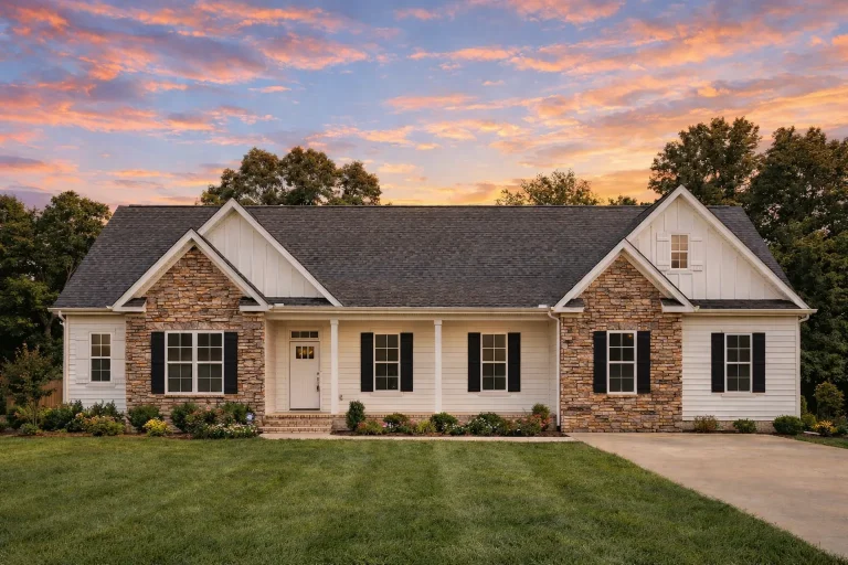 Front view of a Traditional Ranch style home featuring stone and horizontal siding, symmetrical windows, and classic gable rooflines surrounded by lush landscaping