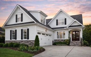 Front elevation of a Transitional Farmhouse home featuring shingle siding, lap siding, stone water table, and black window shutters