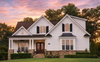 Front elevation of a New American style home with brick and stone exterior, board and batten siding, steep gabled roof, and covered front porch