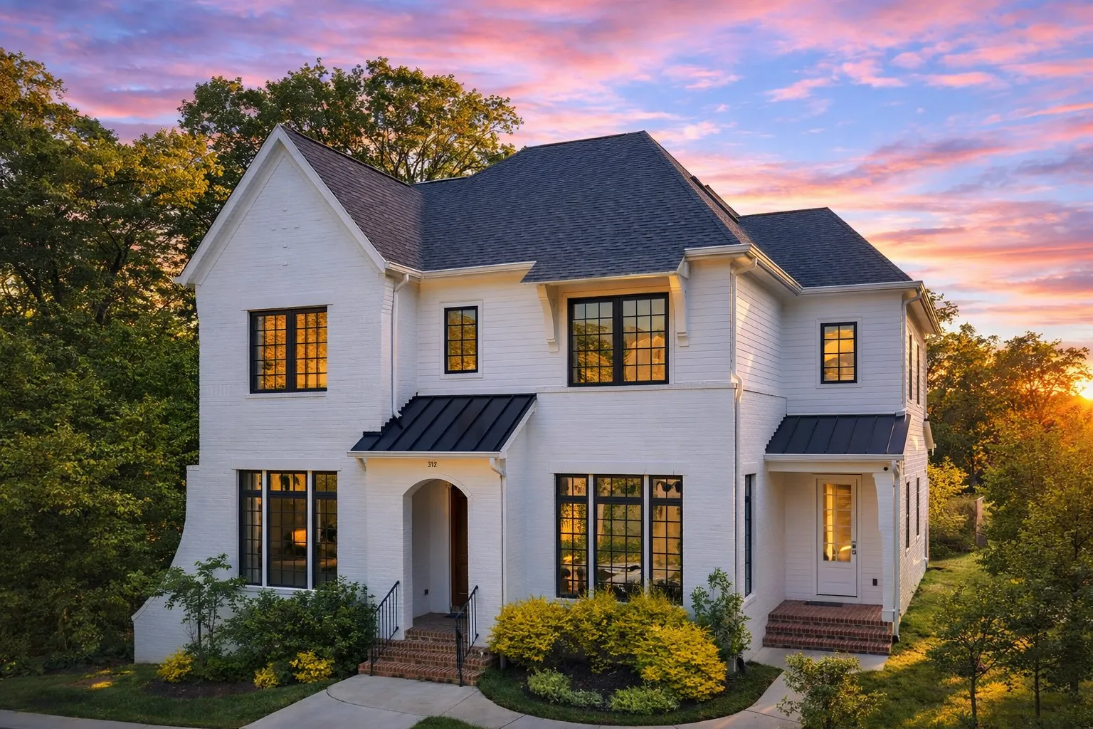 Front elevation of a Modern Farmhouse style home featuring white board and batten siding, black metal awnings, symmetrical windows, and a welcoming covered entry