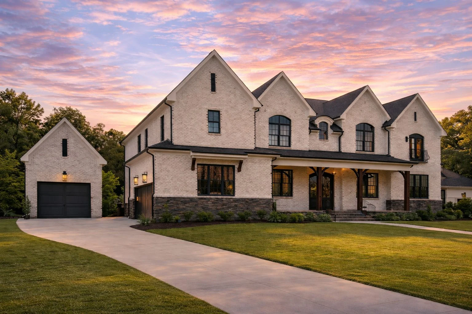 Front view of a French Country style home with painted white brick, stone foundation, black window trim, and wood columns framing the front porch entry