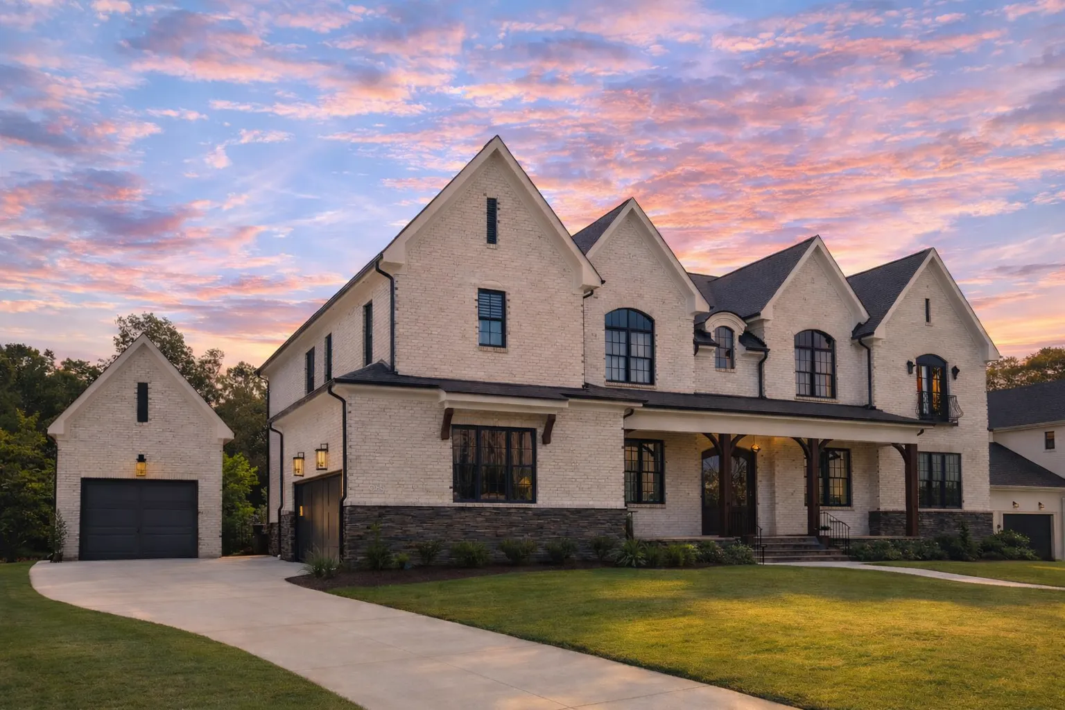 Front view of a French Country style home with painted white brick, stone foundation, black window trim, and wood columns framing the front porch entry