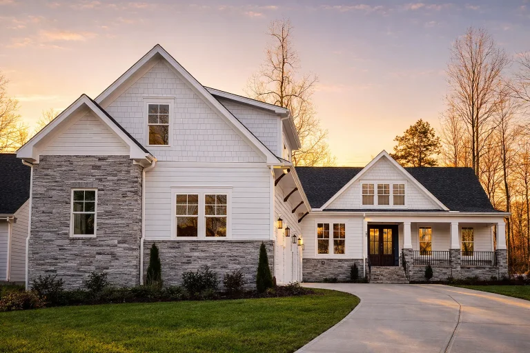 Front exterior of a New American Modern Farmhouse house featuring horizontal siding, stone accents, gabled rooflines, and an inviting covered porch