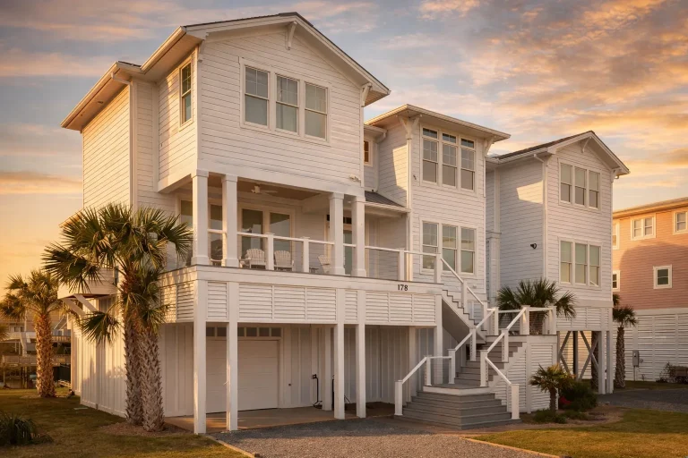 Front elevation of a coastal beach house with raised pier foundation, horizontal lap siding, dual staircases, and large covered porches